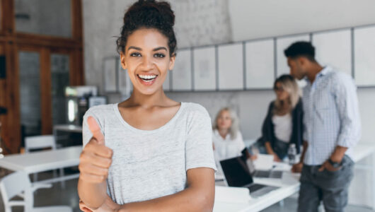 excited-mulatto-woman-with-curly-hairstyle-posing-with-thumb-up-office-stylish-female-african-student-having-fun-after-exams-with-university-friends